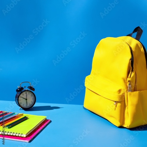 Bright Yellow Backpack With School Supplies on Blue Table at Study Time in th...