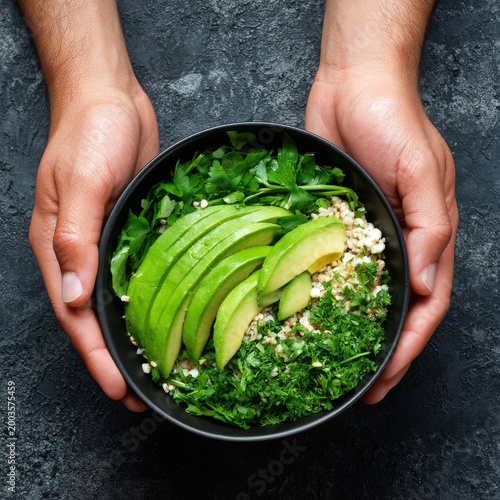 Bowl of Fresh Greens and Avocado Held by Hands Against a Dark Background