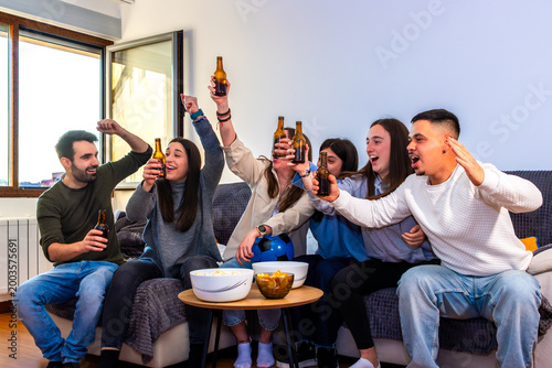 Friends celebrating victory watching football on television at home cheering