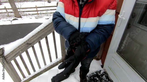 woman putting on winter gloves before shoveling the snow from the stairs after the snow storm in February
