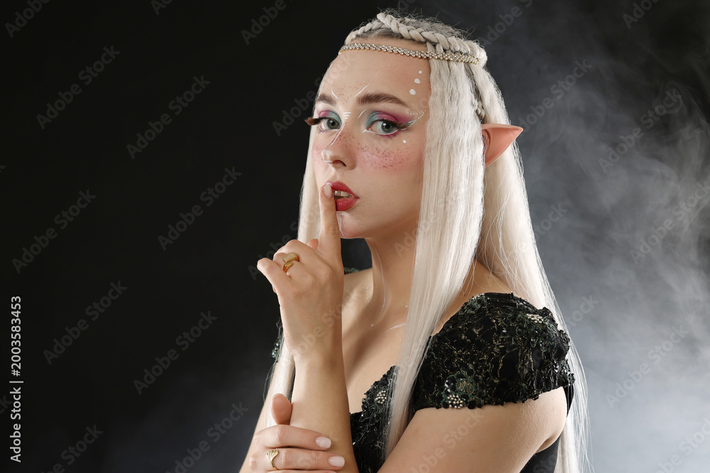 Fototapeta premium Beautiful girl dressed as elf on black background with smoke