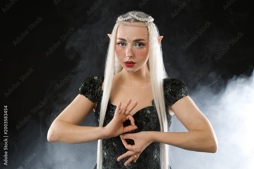 Fototapeta premium Beautiful girl dressed as elf on black background with smoke