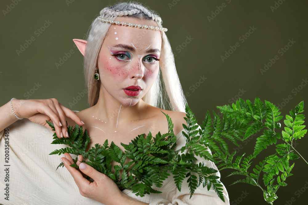 Fototapeta premium Beautiful elf girl with floral decor on dark olive background