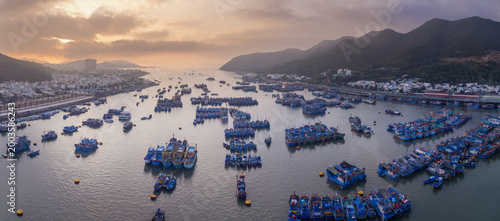An aerial view of Fishing port Vinh Truong, Nha Trang, Vietnam, filled with fishing boats. The boats are moored in the water, with the city skyline visible in the background.