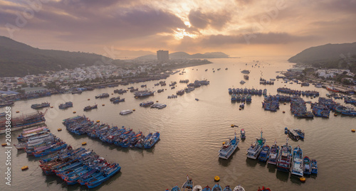 An aerial view of Fishing port Vinh Truong, Nha Trang, Vietnam, filled with fishing boats. The boats are moored in the water, with the city skyline visible in the background.