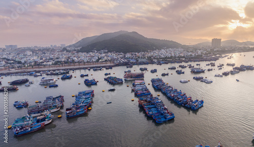 An aerial view of Fishing port Vinh Truong, Nha Trang, Vietnam, filled with fishing boats. The boats are moored in the water, with the city skyline visible in the background.