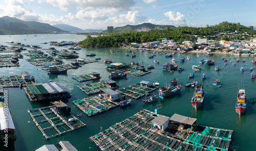 A scenic aerial view of a bustling fishing village in Hon Mieu, Nha Trang, Vietnam, showcasing numerous boats and floating fish farms. 
