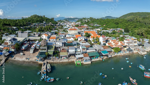 A panoramic view of a coastal village of Hon Mieu, Nha Trang, Vietnam, with traditional fishing boats docked and moored in the turquoise water. 