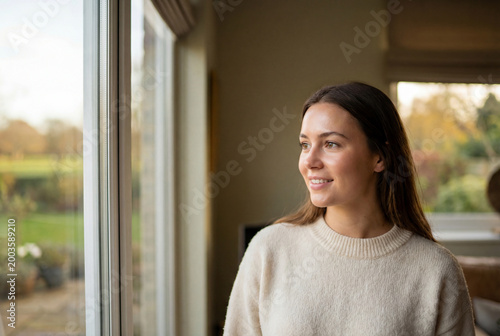 Young woman smiling and gazing out of home window peacefully Free Download Young woman smiling and gazing out of home window peacefully - GFXLoad