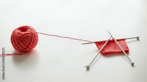 Red yarn ball and knitting needles creating a knitted fabric.