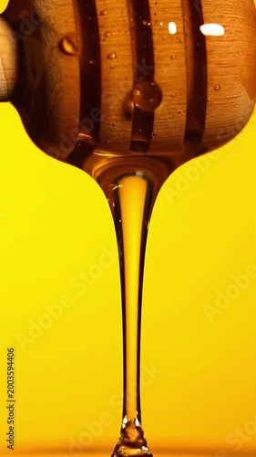 Honey drips from honey dripper on yellow background in close view