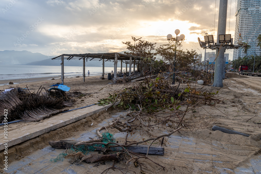 Obraz premium Debris litters a beach in Quy Nhon, Binh Dinh, Vietnam, after a storm. The aftermath shows damaged structures and scattered vegetation along the coastline.