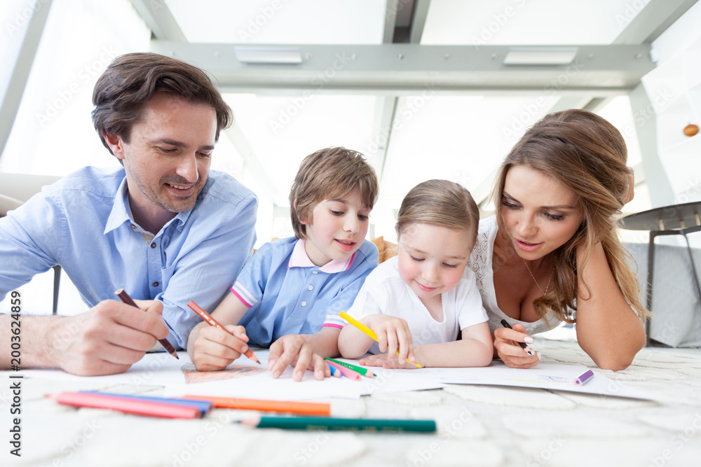 Fototapeta premium Happy family drawing together on the floor in a bright room