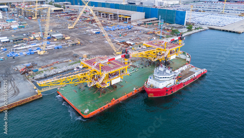 Foto offshore oil and gas platform structure loaded on a heavy transport barge with a supply vessel at a coastal shipyard