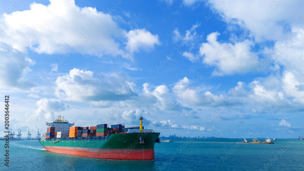 Fototapeta premium Side view of a large green cargo container ship sailing on the sea under a bright blue sky with fluffy white clouds. Global shipping logistics, maritime transport, and international trade.