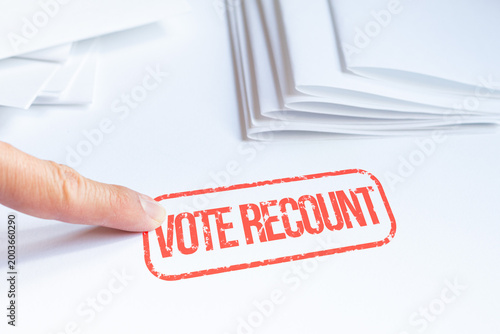 Finger pointing at a Vote Recount stamp next to scattered ballots. Concept of vote recount and verification of election results