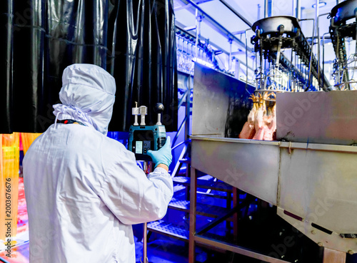 A quality control inspector in white protective gear operating a WBGT heat stress monitor on a chicken processing line to ensure industrial safety compliance.