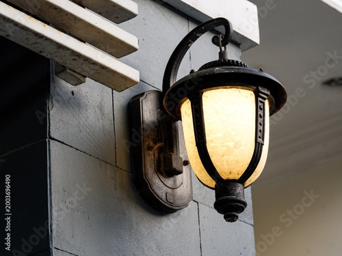 Billede på lærred A classic black metal wall lantern with a warm glowing glass shade mounted on a gray stone wall