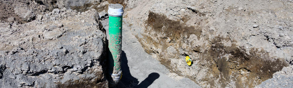 Fototapeta premium Residential construction site earthwork, trench dug in ground with 6 inch pipe installed and pipe plug, seal pipe, to cap ends, housing development 