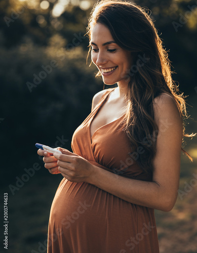 Joyful Expectation: A radiant, pregnant woman holds a pregnancy test, her face alight with happiness, embodying the beauty of anticipation and maternal bond.