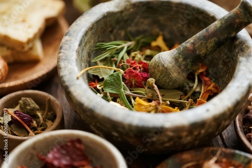 Herbal ingredients in a stone mortar and pestle with dried flowers, leaves, and spices