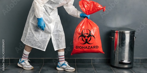 Person in Protective Suit Handling Biohazard Waste Bag Representing Medical Safety Hazard Disposal Infection Control and Laboratory Protection Concept