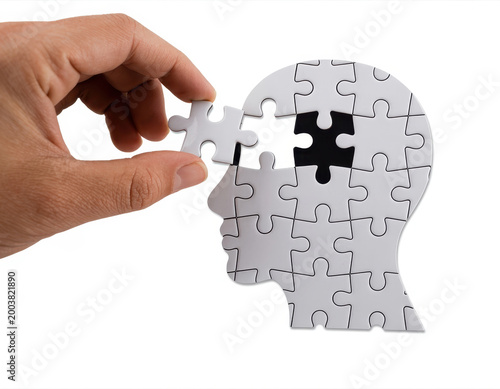Hand placing a puzzle piece into a human head shape made of jigsaw pieces on white background view