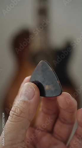 Close-up of a hand holding a guitar pick with a blurred guitar in the background