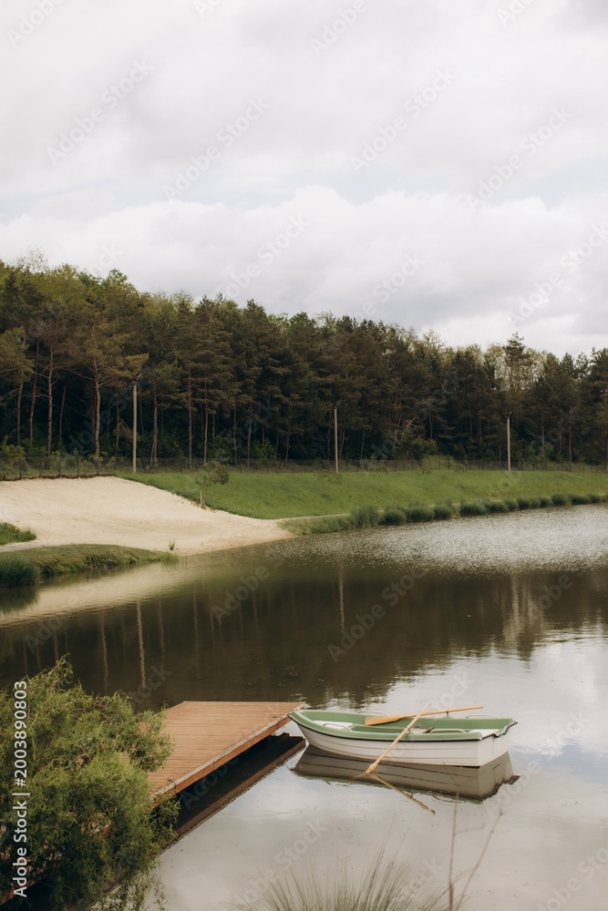Fototapeta premium Rowboat tethered to pier on serene lake reflecting forest