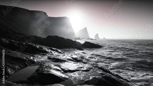 Dramatic black and white landscape of ocean waves crashing against rocky coastline under a bright sun
