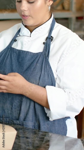 Vertical video: Accepting customer phone, chef in coat and denim apron adjusting box at bakery POS