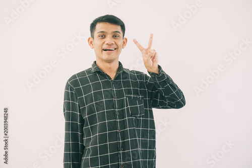 Slika na platnu a man wearing a black and white plaid shirt stands against a plain white background, his right hand raised in a peace sign gesture