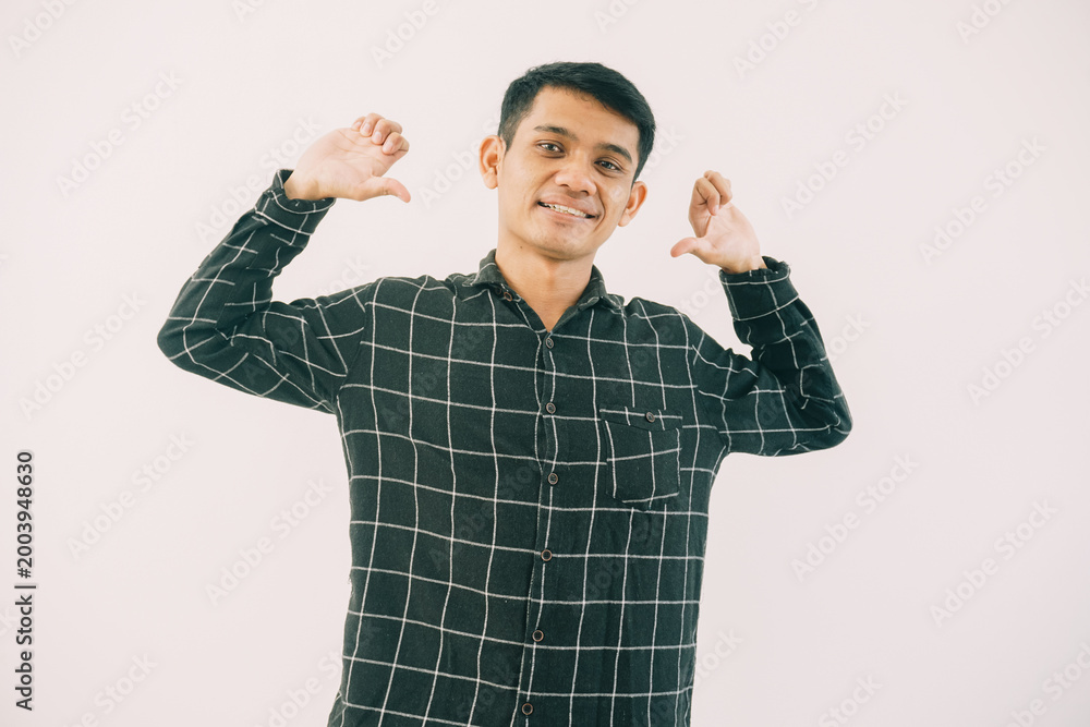 Naklejka premium young asian male wearing dark green and black checkered long-sleeve shirt, hands raised in peace sign. bright even lighting with clean white background ideal for advertising and social media content.