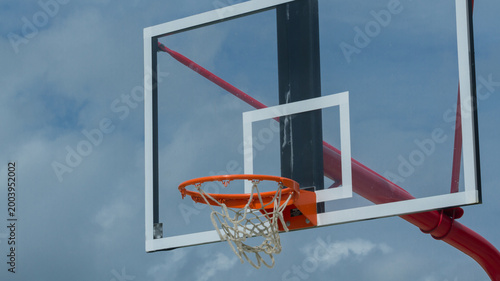 Photography Outdoor basketball hoop with orange rim and transparent backboard against cloudy