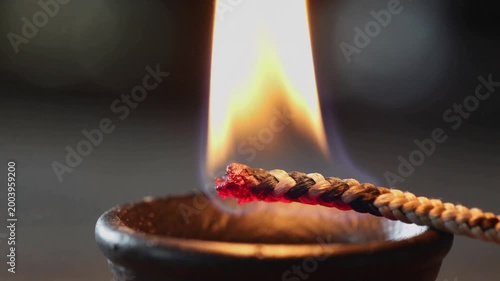 Close-up of a lit agarbatti stick in a small metal holder with a warm flame and dark background.