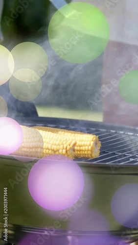 Vertical video: Two men handling tongs placing second corn on grill, smoke rising, cooking barbecue