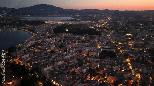Aerial Night Cityscape of Corfu Town and Bay Area with Glowing Streetlights and Distant Airport, Greece