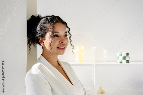 Smiling confidant woman leaning against white wall in modern office