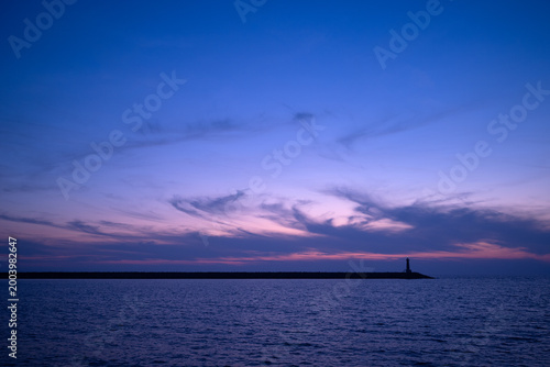 Φωτογραφία Lighthouse on horizon during blue hour over calm sea