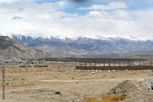 A wide view of a dry valley and a small town, backed by beautiful snow-capped mountains in Ladakh,India.