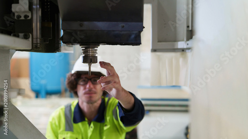 фотографія Male worker in yellow safety vest meticulously inspects CNC machine spindle with tablet, performing precision maintenance and quality control in modern factory environment