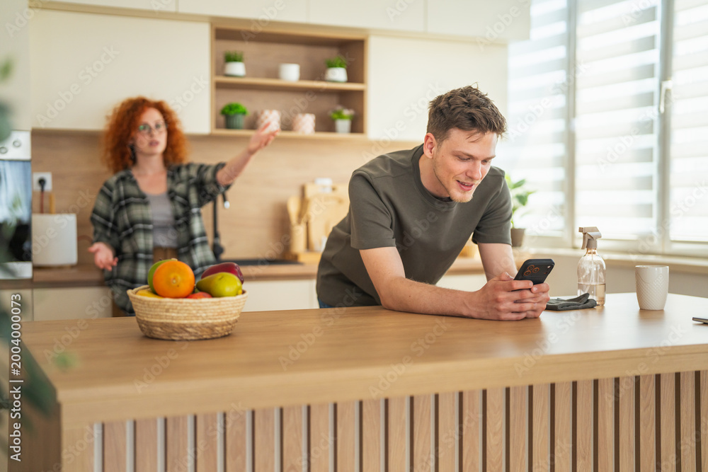 Φωτογραφία Man ignoring woman arguing using smart phone in kitchen