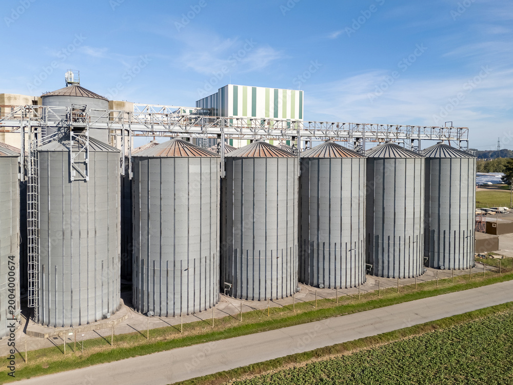 Fototapeta premium Grain silos stand tall in a storage facility surrounded by fields. This aerial view shows their structure and layout.