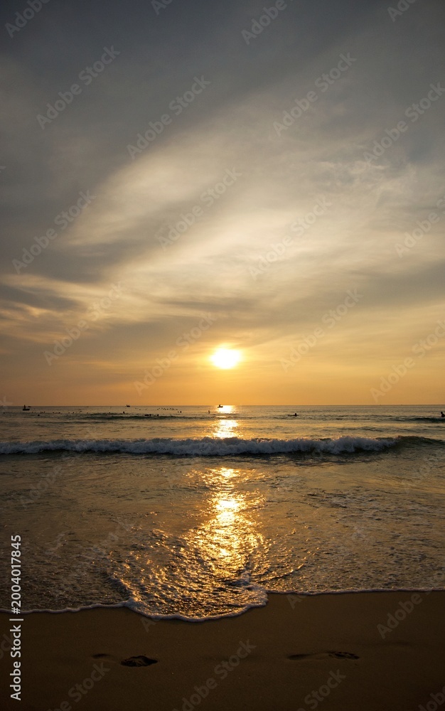 Fototapeta premium Scenic golden sunset over tropical beach with gentle ocean waves and glowing sun reflections on the sand