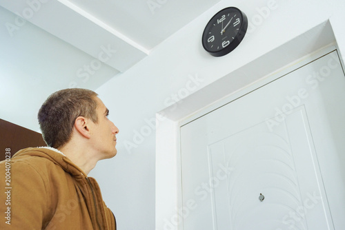 Fotografija Man looking up at wall clock beside apartment entrance door before leaving home