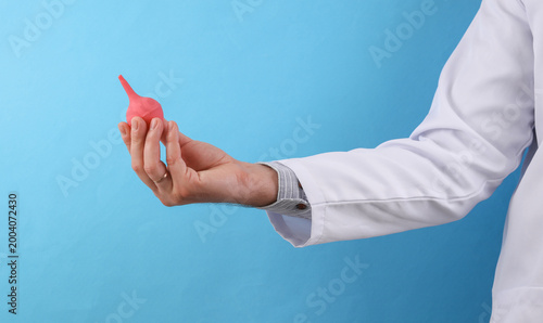 Schilderij op canvas Doctor in a white medical coat holding  enema on a blue background