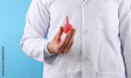 Fotografía Doctor in a white medical coat holding  enema on a blue background