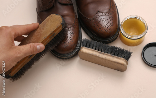 Foto Man's hand takes care of leather shoes on a beige background