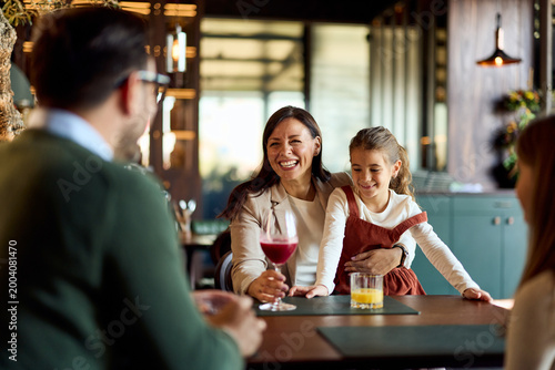 Smiling Mother and Daughter Sharing Drinks and Laughs While Dining With Friends in Cozy Restaurant