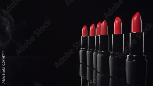 Cinematic panning shot of vibrant red lipsticks lined up against a dark background with subtle smoke wisps, symbolizing beauty, glamour, and feminine allure in cosmetic advertising and lifestyle